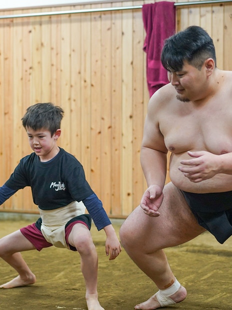 Child practicing sumo wrestling with a sumo wrestler in Tokyo dojo.