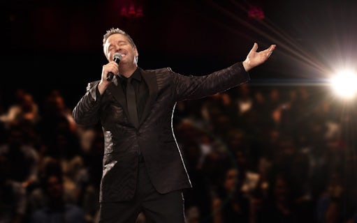 Entertainer performing on stage with microphone, spotlight, and audience in background.