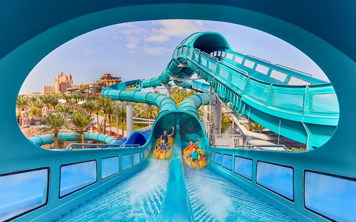 Riders on Medusas Lair water slide at Atlantis, The Palm, Dubai with resort view.