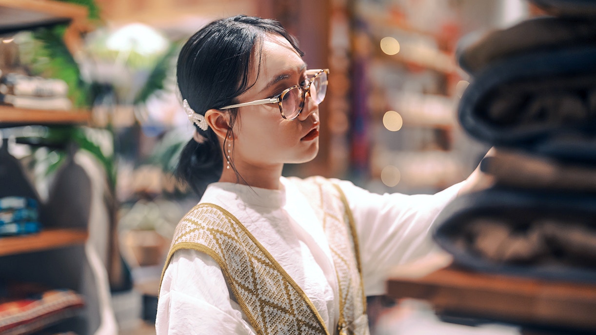Woman browsing folded clothes in a store.