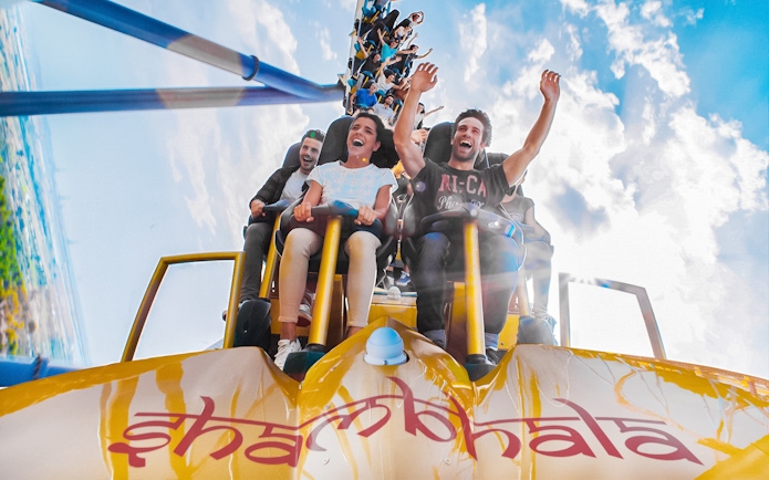 Tourists on Shambhala roller coaster at PortAventura, Spain, with arms raised in excitement.