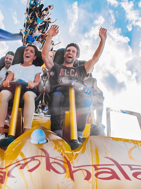 Tourists on Shambhala roller coaster at PortAventura, Spain, with arms raised in excitement.