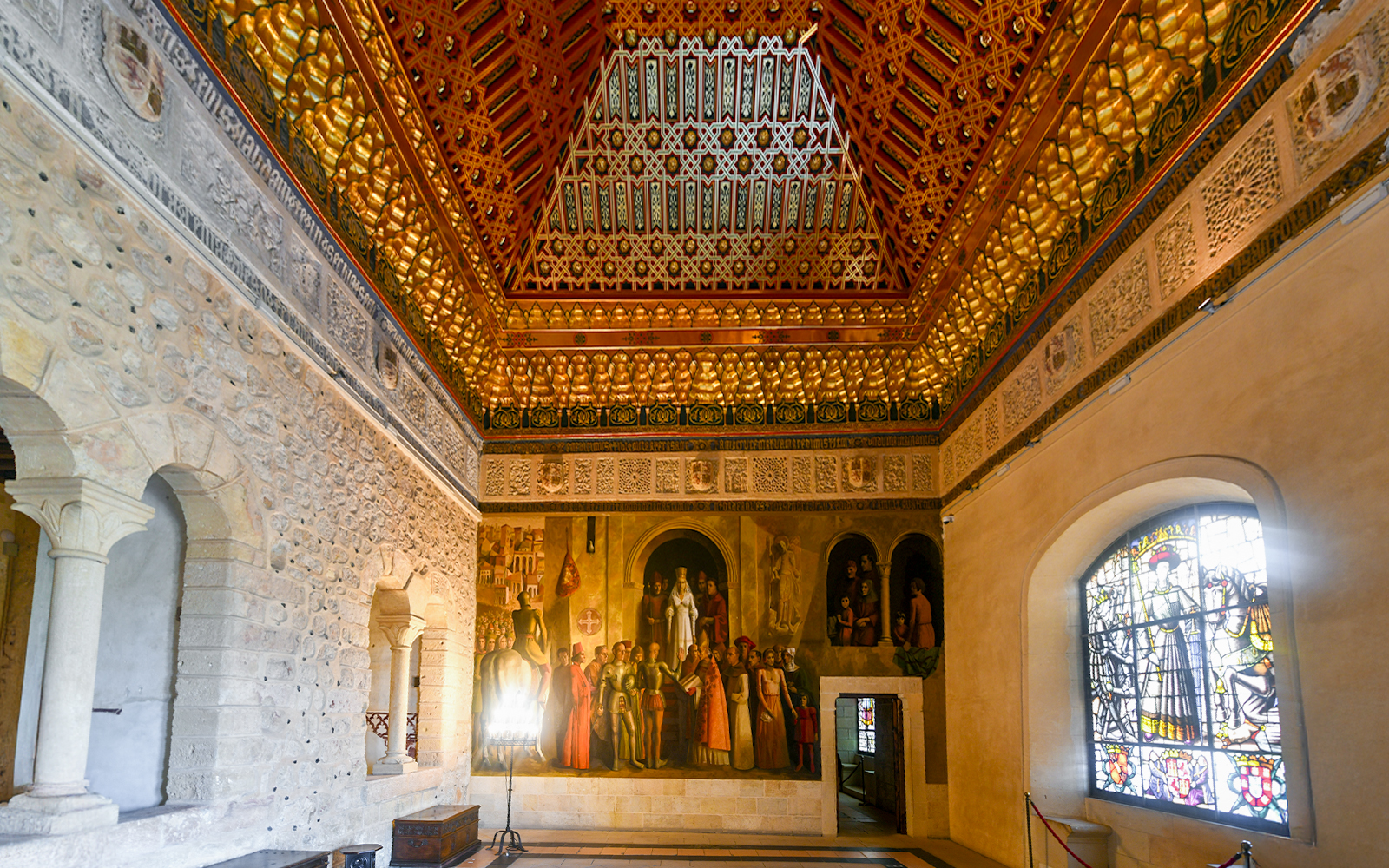 Interior of Alcazar of Segovia, Spain, featuring ornate ceiling, mural, and stained glass window.