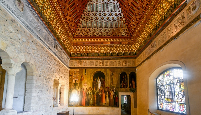 Interior of Alcazar of Segovia, Spain, featuring ornate ceiling, mural, and stained glass window.