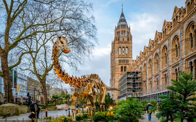 Dinosaur sculpture outside Natural History Museum, London, with historic architecture in the background.