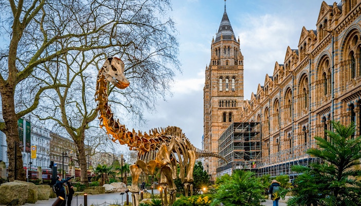 Dinosaur sculpture outside Natural History Museum, London, with historic architecture in the background.