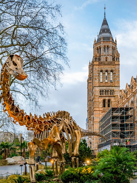 Dinosaur sculpture outside Natural History Museum, London, with historic architecture in the background.