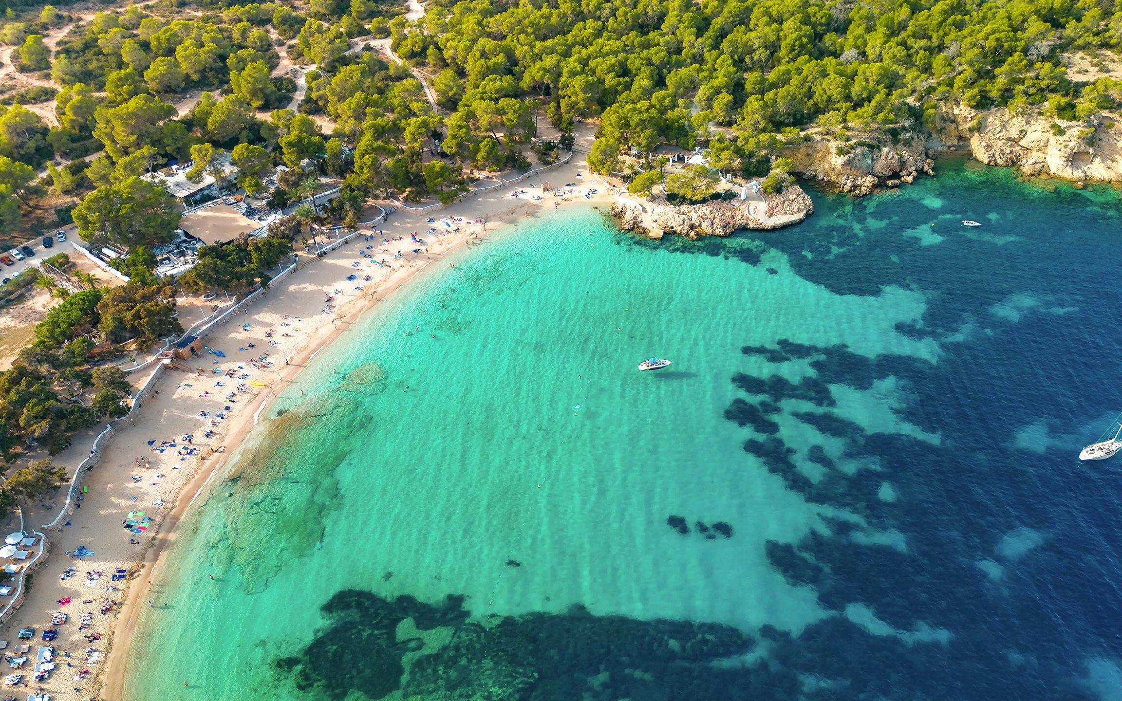 Aerial view of Cala Bassa Beach with turquoise waters and surrounding greenery in Ibiza, Spain.