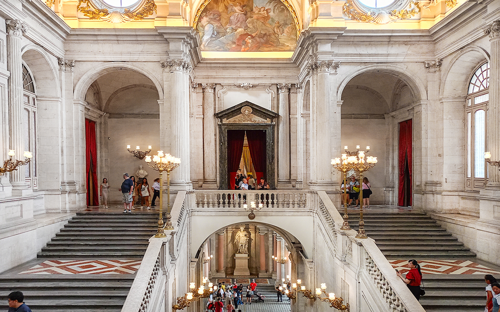 Royal Palace of Madrid grand staircase with visitors exploring the ornate interior.