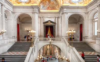 Royal Palace of Madrid grand staircase with visitors exploring the ornate interior.