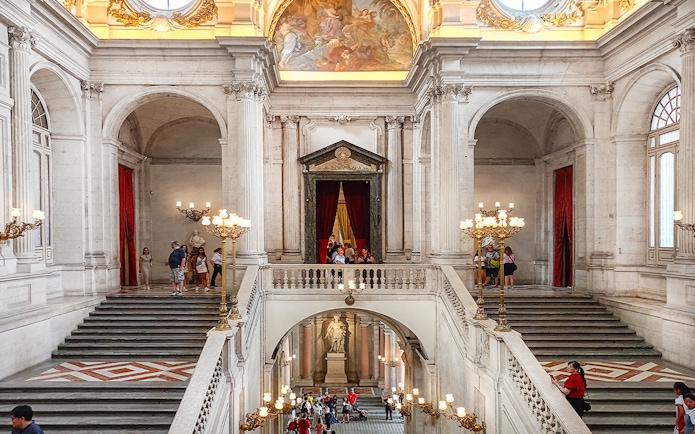 Royal Palace of Madrid grand staircase with visitors exploring the ornate interior.