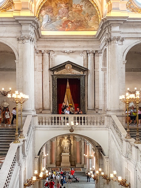 Royal Palace of Madrid grand staircase with visitors exploring the ornate interior.