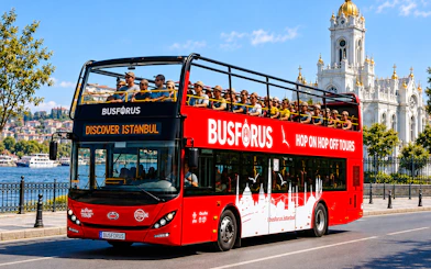 Open-top tour bus in Istanbul with passengers, passing by the Bosphorus and a historic church.