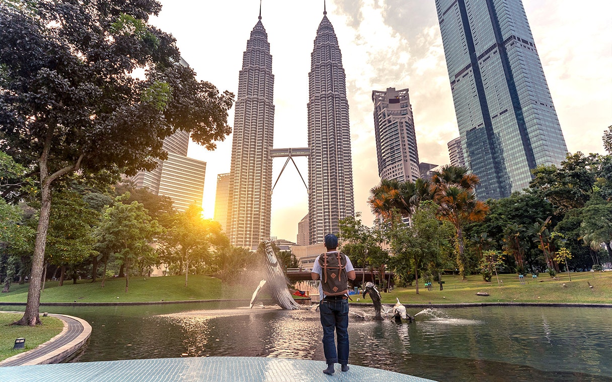 Traveler at Petronas Towers, Kuala Lumpur, with sunset and fountain in the foreground.