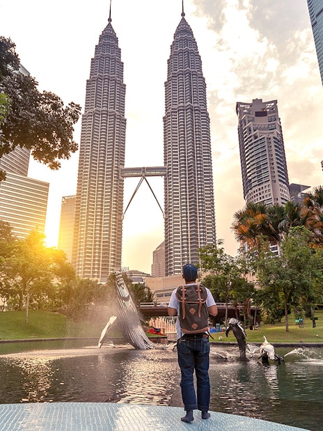 Traveler at Petronas Towers, Kuala Lumpur, with sunset and fountain in the foreground.