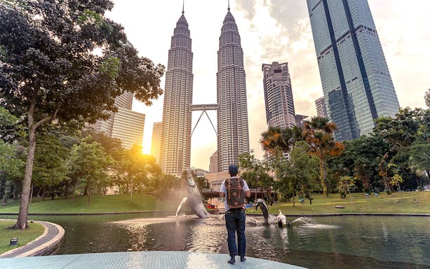 Traveler at Petronas Towers, Kuala Lumpur, with sunset and fountain in the foreground.