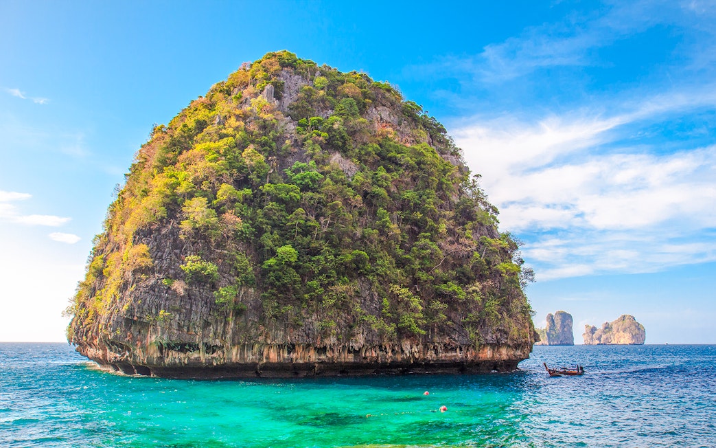Limestone cliff and turquoise water at Loh Samah Bay, Krabi, with a traditional boat nearby.