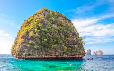 Limestone cliff and turquoise water at Loh Samah Bay, Krabi, with a traditional boat nearby.