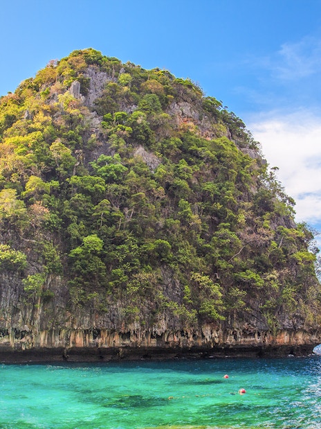 Limestone cliff and turquoise water at Loh Samah Bay, Krabi, with a traditional boat nearby.