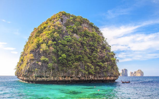 Limestone cliff and turquoise water at Loh Samah Bay, Krabi, with a traditional boat nearby.