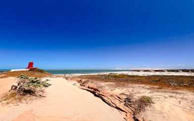 Red lighthouse on sandy dunes overlooking the ocean at Pontal de Maceió, Fortim.