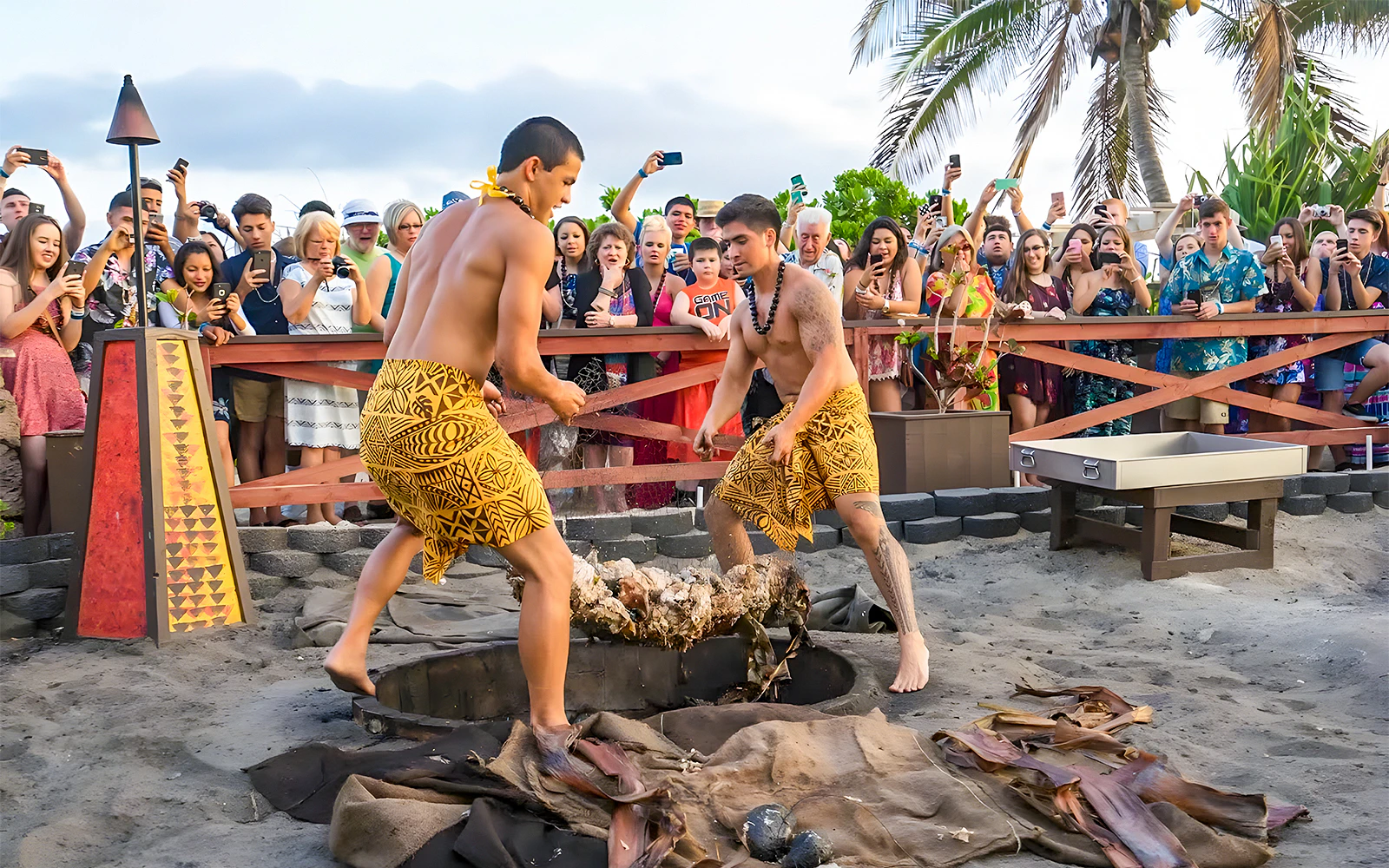 Men in traditional attire preparing a pig for roasting at Germaine's Luau, Hawaii, with a crowd watching.