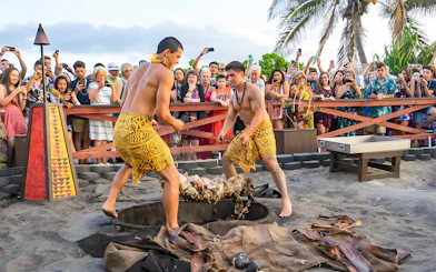 Men in traditional attire preparing a pig for roasting at Germaine's Luau, Hawaii, with a crowd watching.