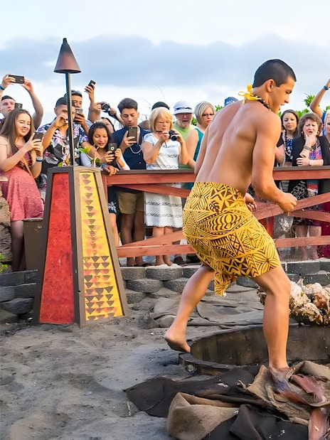 Men in traditional attire preparing a pig for roasting at Germaine's Luau, Hawaii, with a crowd watching.
