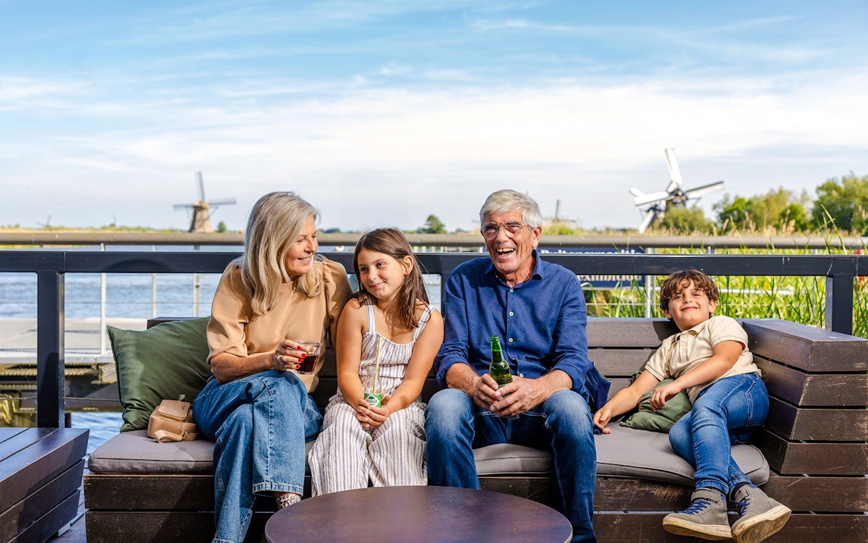 Family relaxing on a bench with Kinderdijk windmills in the background.