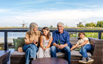 Family relaxing on a bench with Kinderdijk windmills in the background.