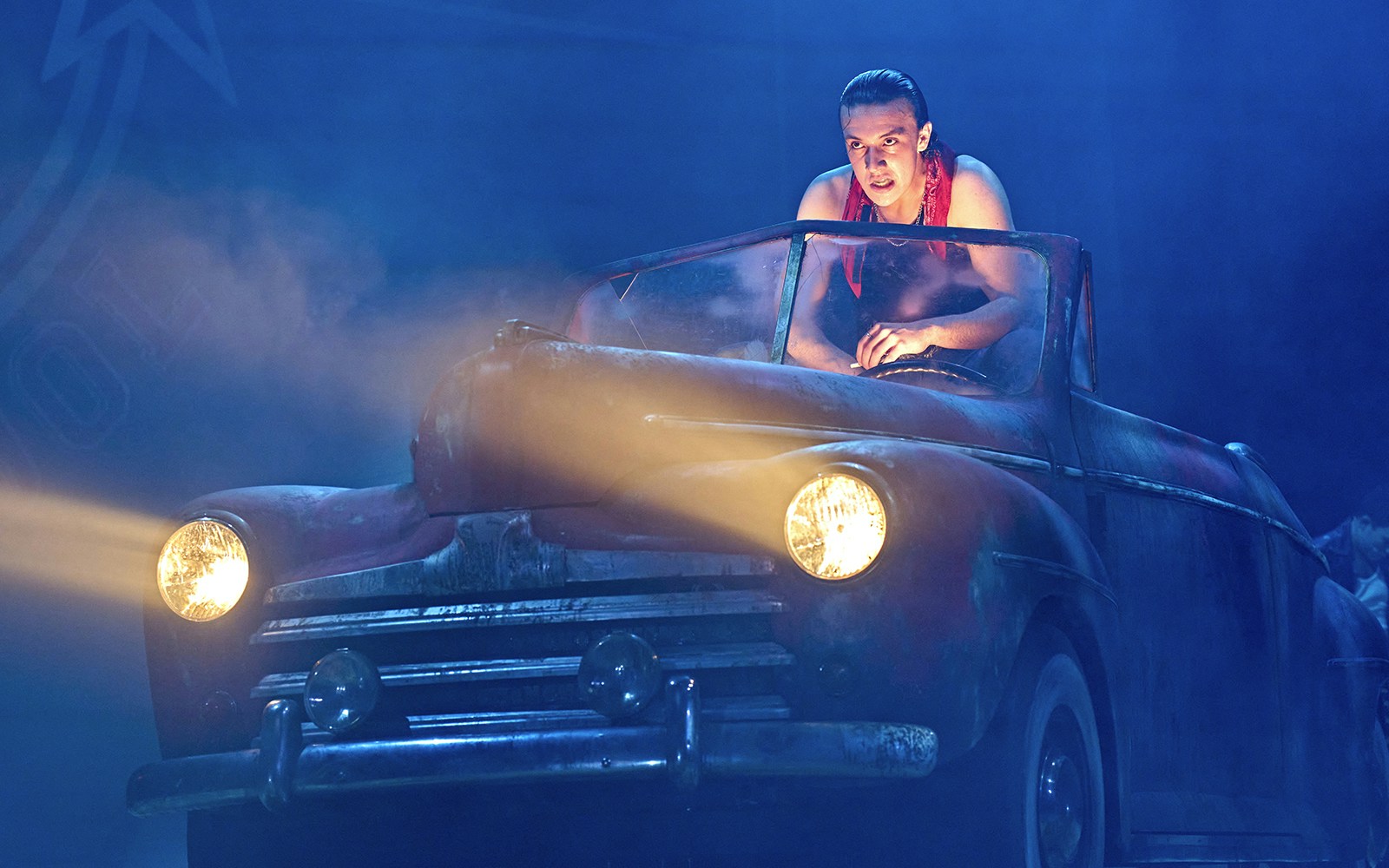 Person in a vintage car on stage during a Grease performance.