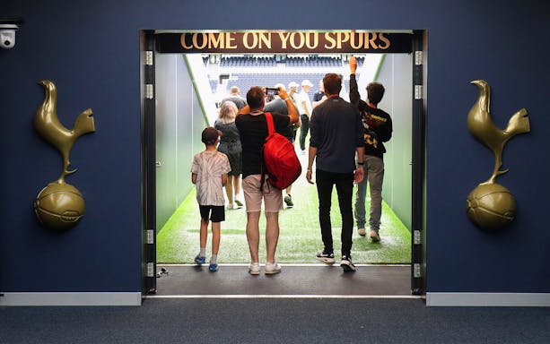 Visitors entering Tottenham Hotspur Stadium tunnel with "Come On You Spurs" sign.