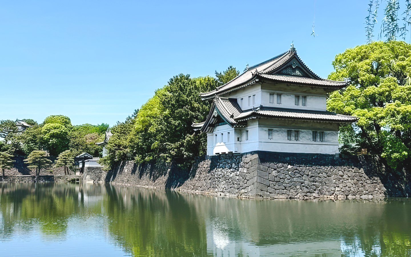 Imperial Palace building by a moat in Tokyo, surrounded by lush greenery.