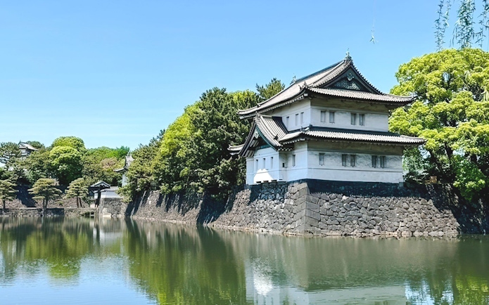Imperial Palace building by a moat in Tokyo, surrounded by lush greenery.