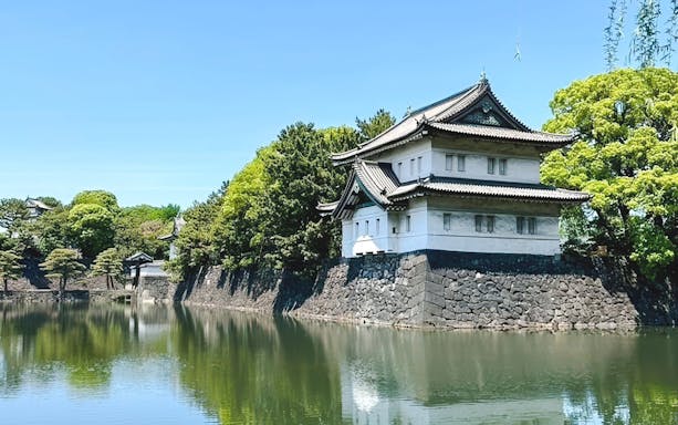 Imperial Palace building by a moat in Tokyo, surrounded by lush greenery.