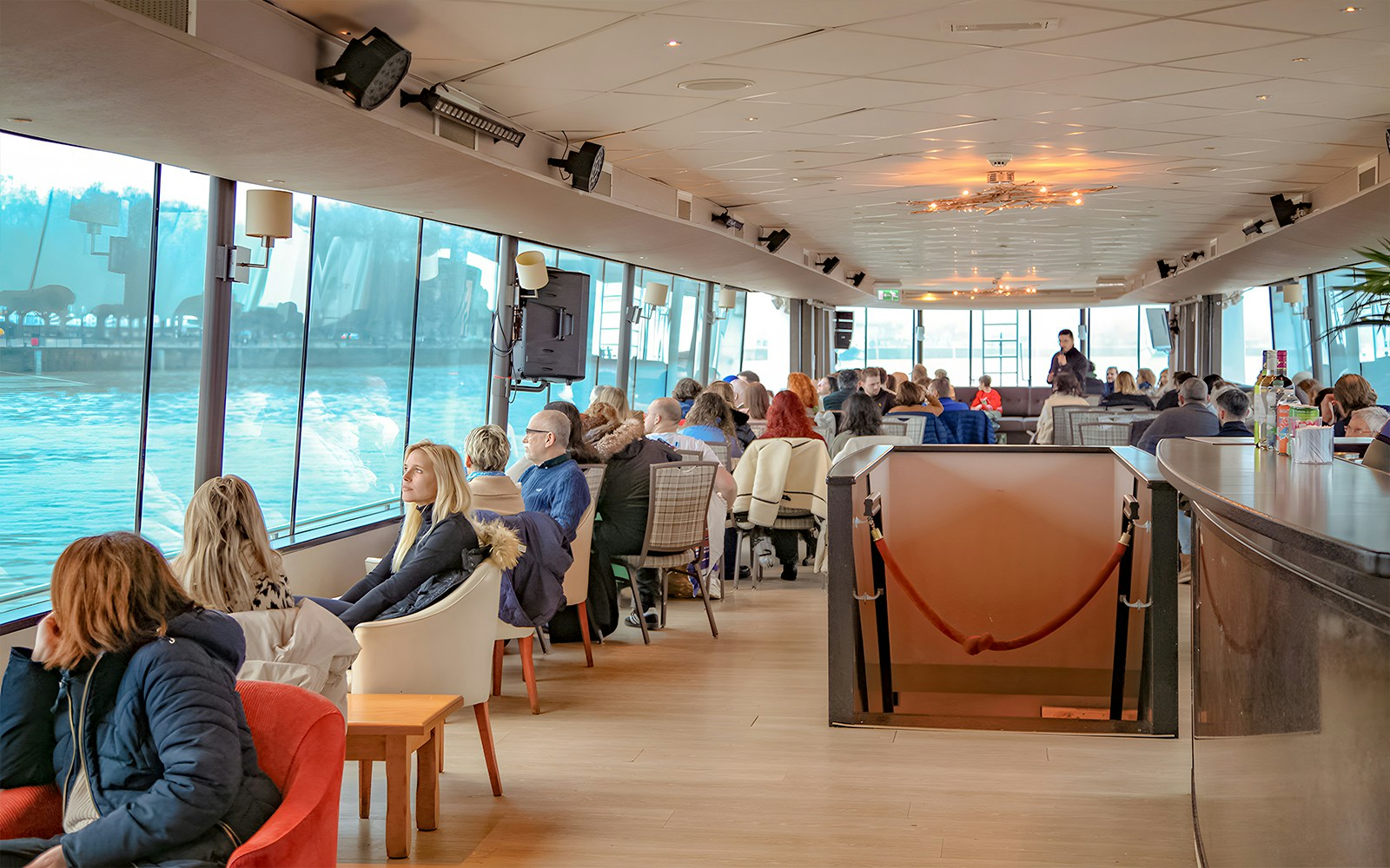 People enjoying a scenic Bordeaux river cruise inside a boat with large windows.