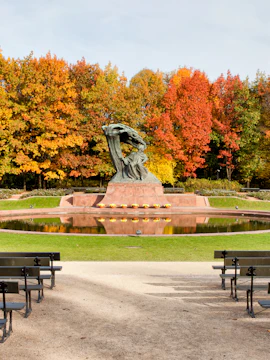 Chopin monument in Warsaw's Łazienki Park with autumn trees in the background.