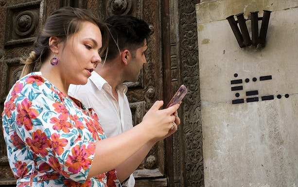 Visitors engaging in a city game in Nice's Old Town, examining a wall with artistic symbols.