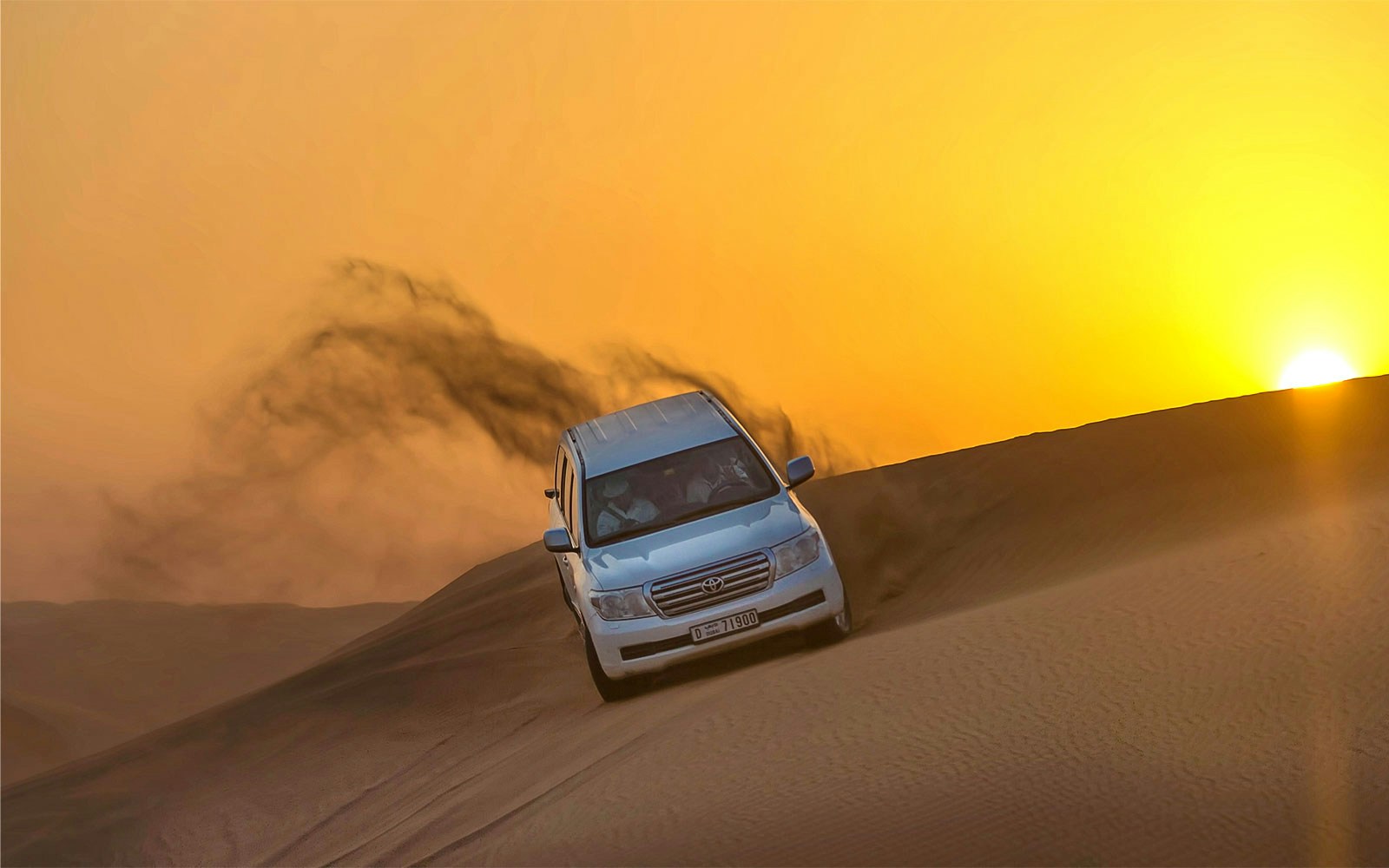 Tourists in a 4x4 vehicle driving through Dubai desert at sunset.
