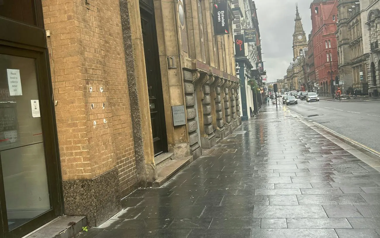 Wet street in Liverpool with historic buildings and clock tower, part of self-guided city exploration game.