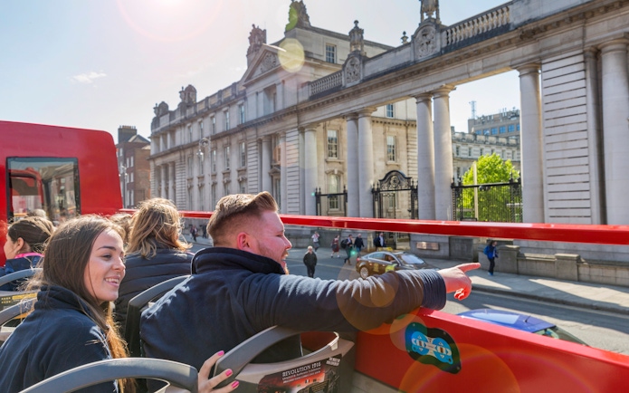 Open-top tour bus passengers view historic Dublin architecture.