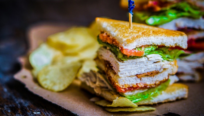 Club sandwich with turkey, lettuce, and tomato, served with potato chips.