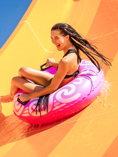 Woman enjoying a water slide on a pink inflatable at a water park.