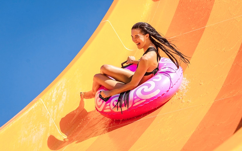 Woman enjoying a water slide on a pink inflatable at a water park.
