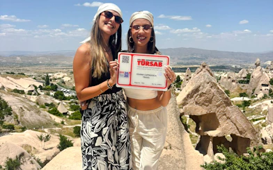 Two people holding a tour sign with Cappadocia rock formations in the background.