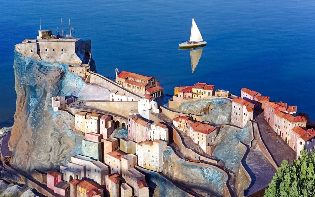 Italia in Miniatura model of coastal village with sailboat on blue water.