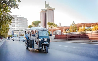 Electric tuk-tuk on Paseo de la Castellana, Madrid, with Torres de Colón in the background.