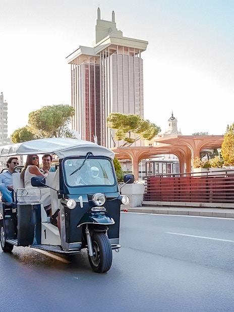 Electric tuk-tuk on Paseo de la Castellana, Madrid, with Torres de Colón in the background.