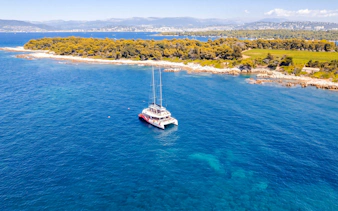 Catamaran cruising near Lérins Island, Marina Bay of Angels, with coastal landscape.