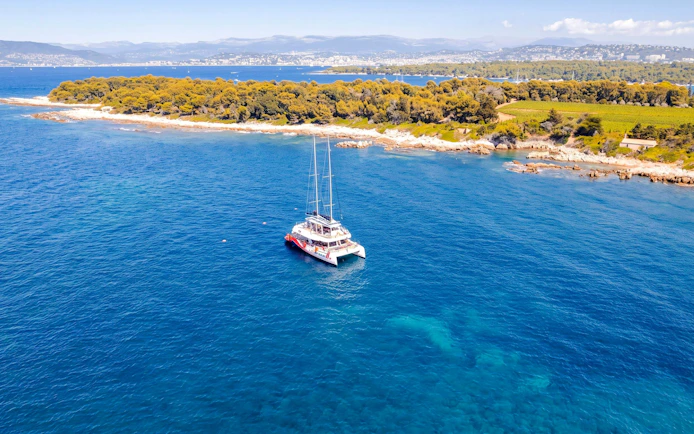 Catamaran cruising near Lérins Island, Marina Bay of Angels, with coastal landscape.